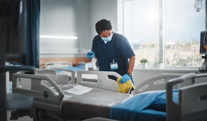 Hospital Ward: Professional Black Nurse Wearing Face Mask, Wiping the Bed, Cleaning Room After Covid-19 Patients Recover. Disinfection, Sterilizing, Sanitizing Clinic after Coronavirus Infected People 