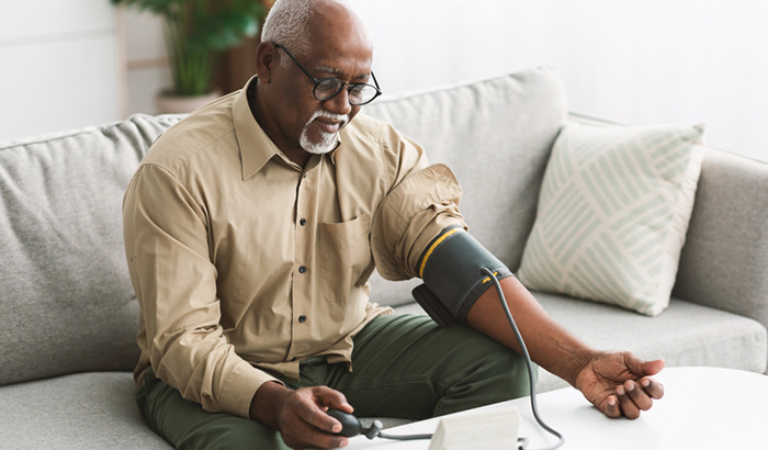 Senior African American Male Measuring Arterial Blood Pressure Having Hypertension Symptom Sitting On Couch At Home. High Blood-Pressure, Health Problem Concept 