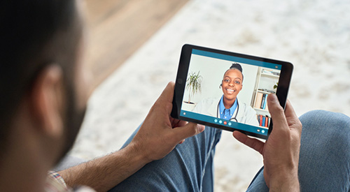 Man having videocall videoconference at home with black female doctor therapist using tablet computer. Online virtual telemedicine health care concept.